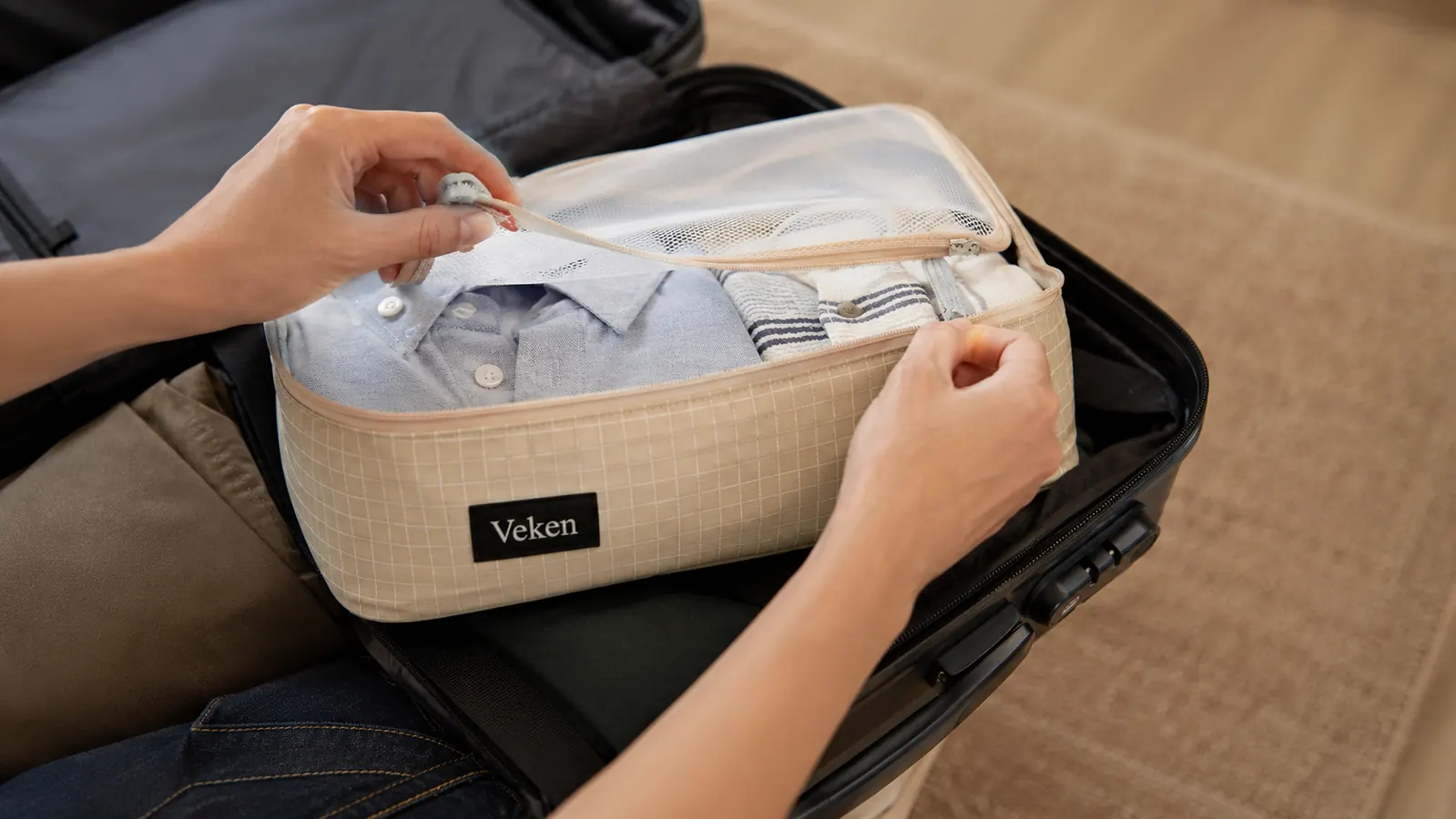 Hand holding a Veken packing cube with the double zipper open showing clothing compressed inside